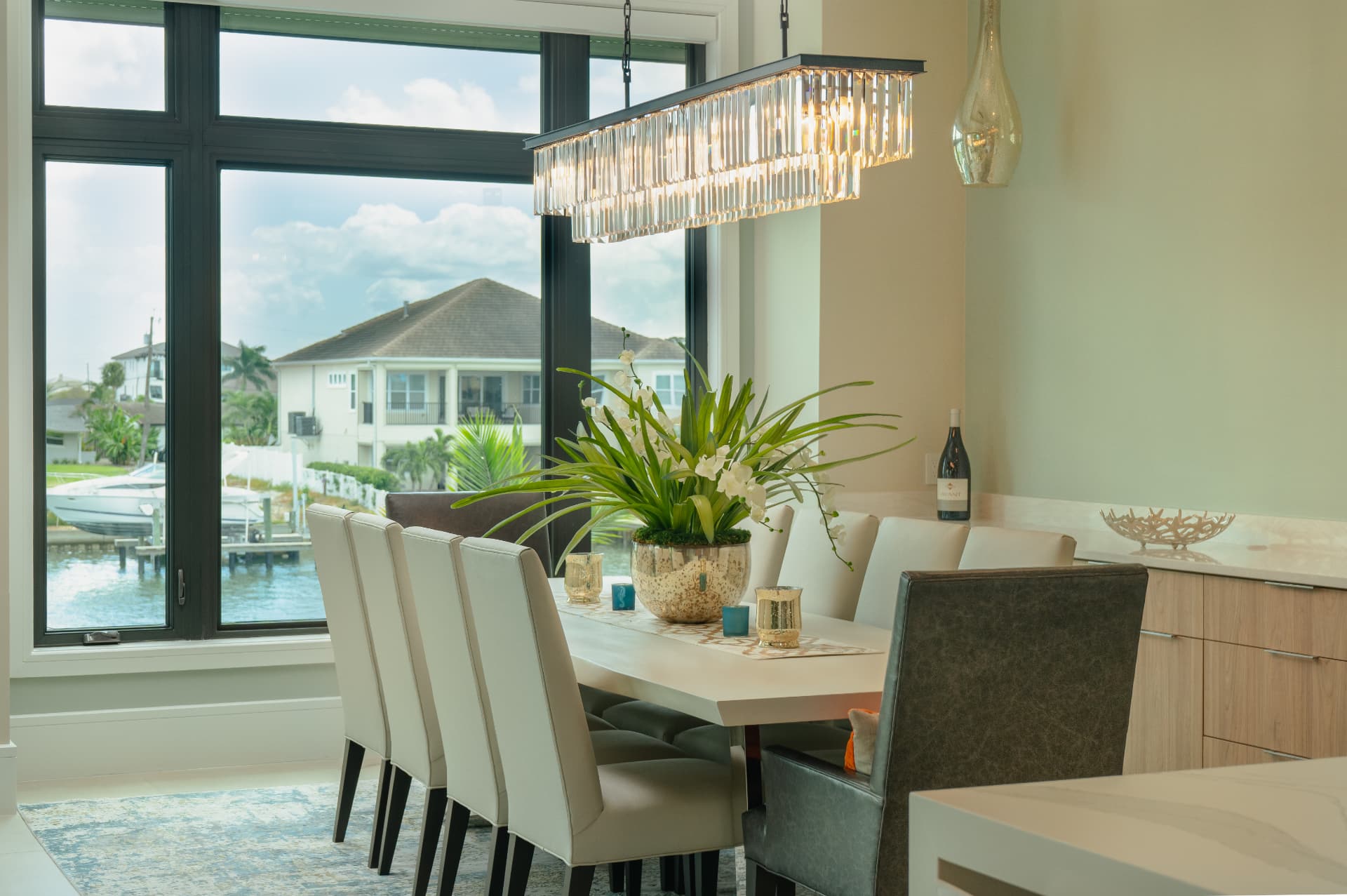 Dining room with pale chairs, a sculptural chandelier, and large garden-facing windows