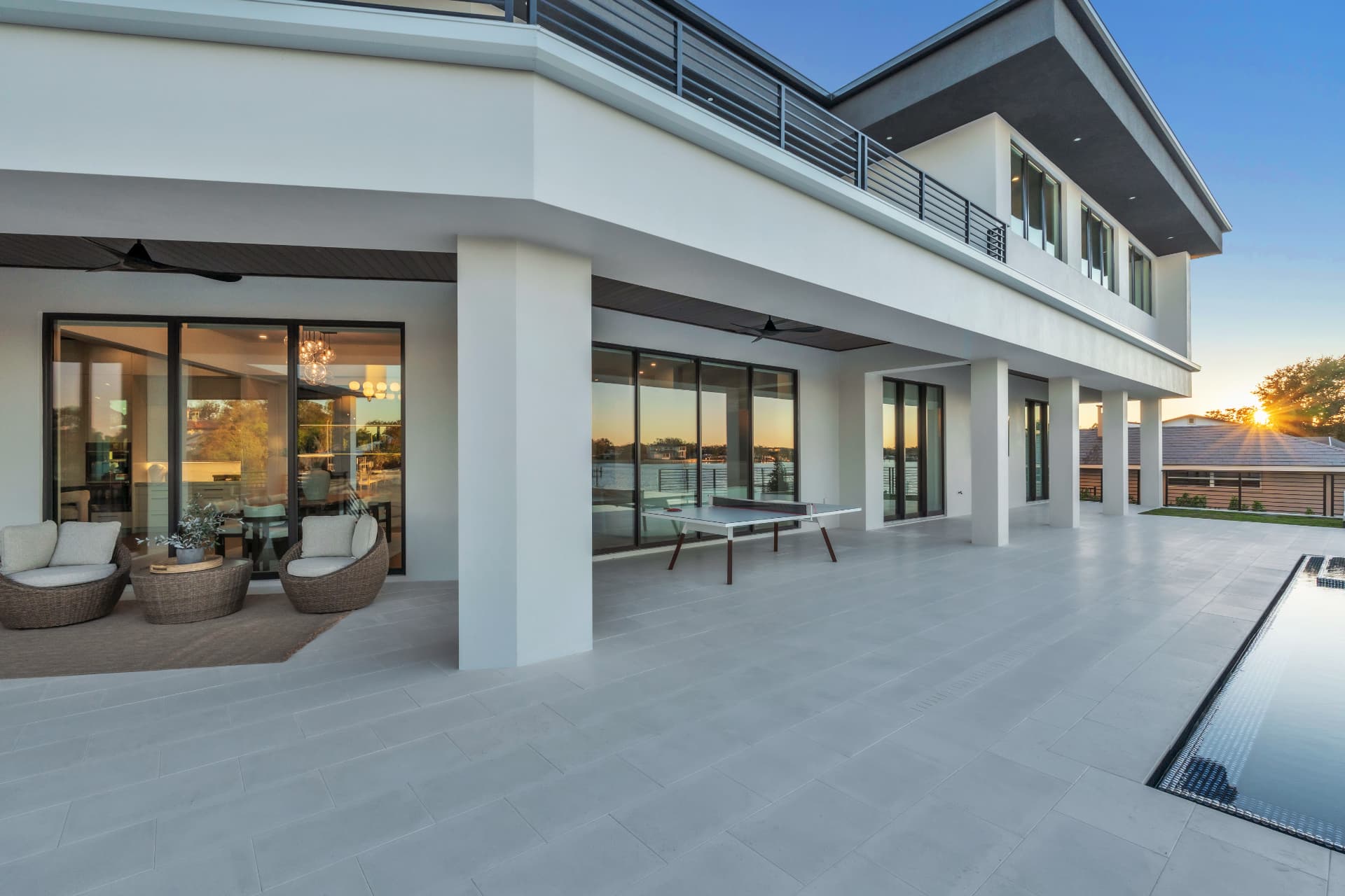 Waterfront home's white exterior and wide terrace framed by sliding glass doors