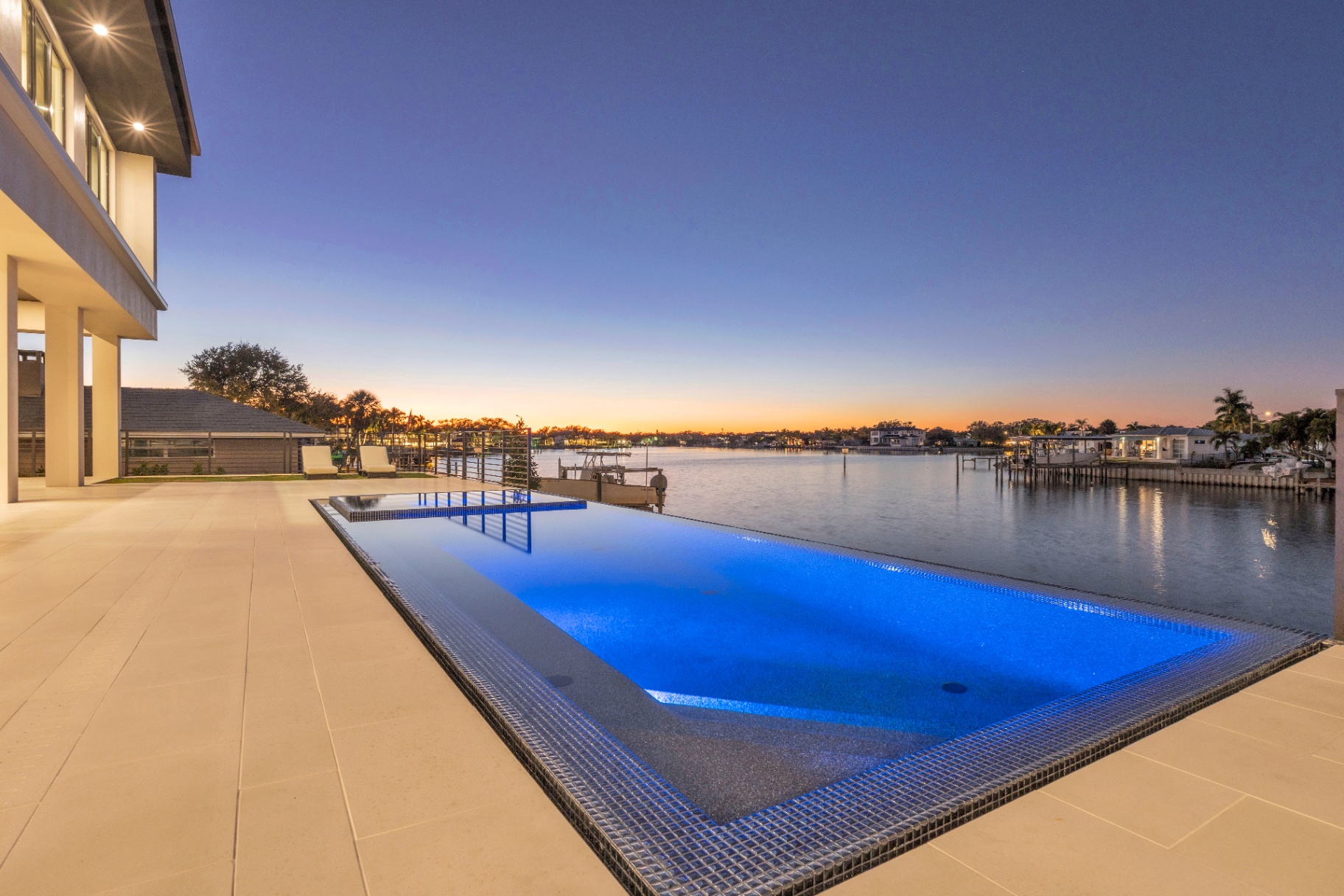 Waterfront home's terrace and illuminated pool at dusk